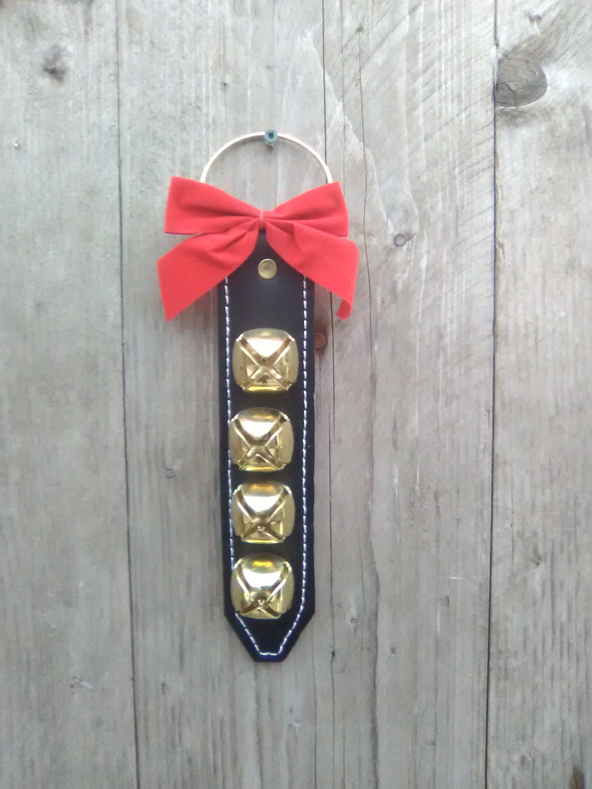 This door hanger is not only decorative but can help serve a purpose. You can hang it on a residential internal or external door, a commercial entrance, hang on a walker, for instance. The bells ring when in motion. The thick black harness leather is stitched and lined with brown garment leather. The brass plated bells and ring are riveted onto the leather. Attached is also a red bow. Made in Kirkfield, Ont. Door hanger with 4 brass plated bells - Brown Leather