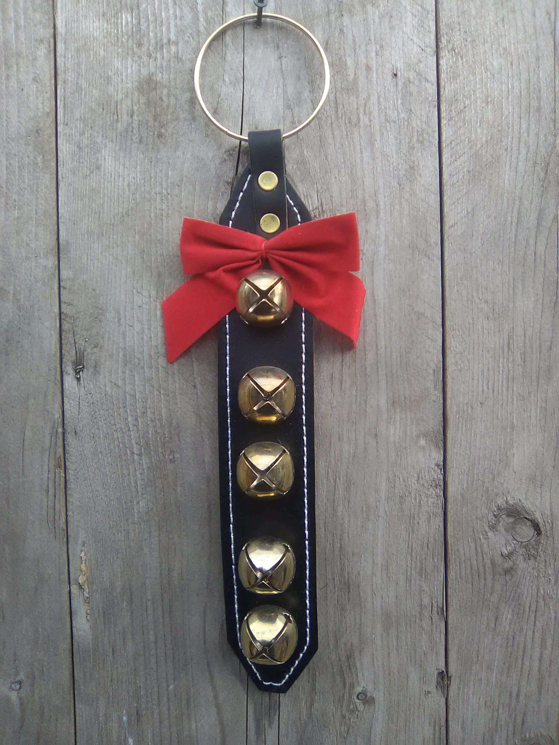 This door hanger is not only decorative but can help serve a purpose. You can hang it on a residential internal or external door, a commercial entrance, for instance. The bells ring when in motion. The thick black harness leather is stitched and lined with garment leather. The brass plated bells and ring are riveted onto the leather. Attached is also a red bow. Made in Kirkfield, Ont. Door hanger with 5 brass plated bells - Black Leather