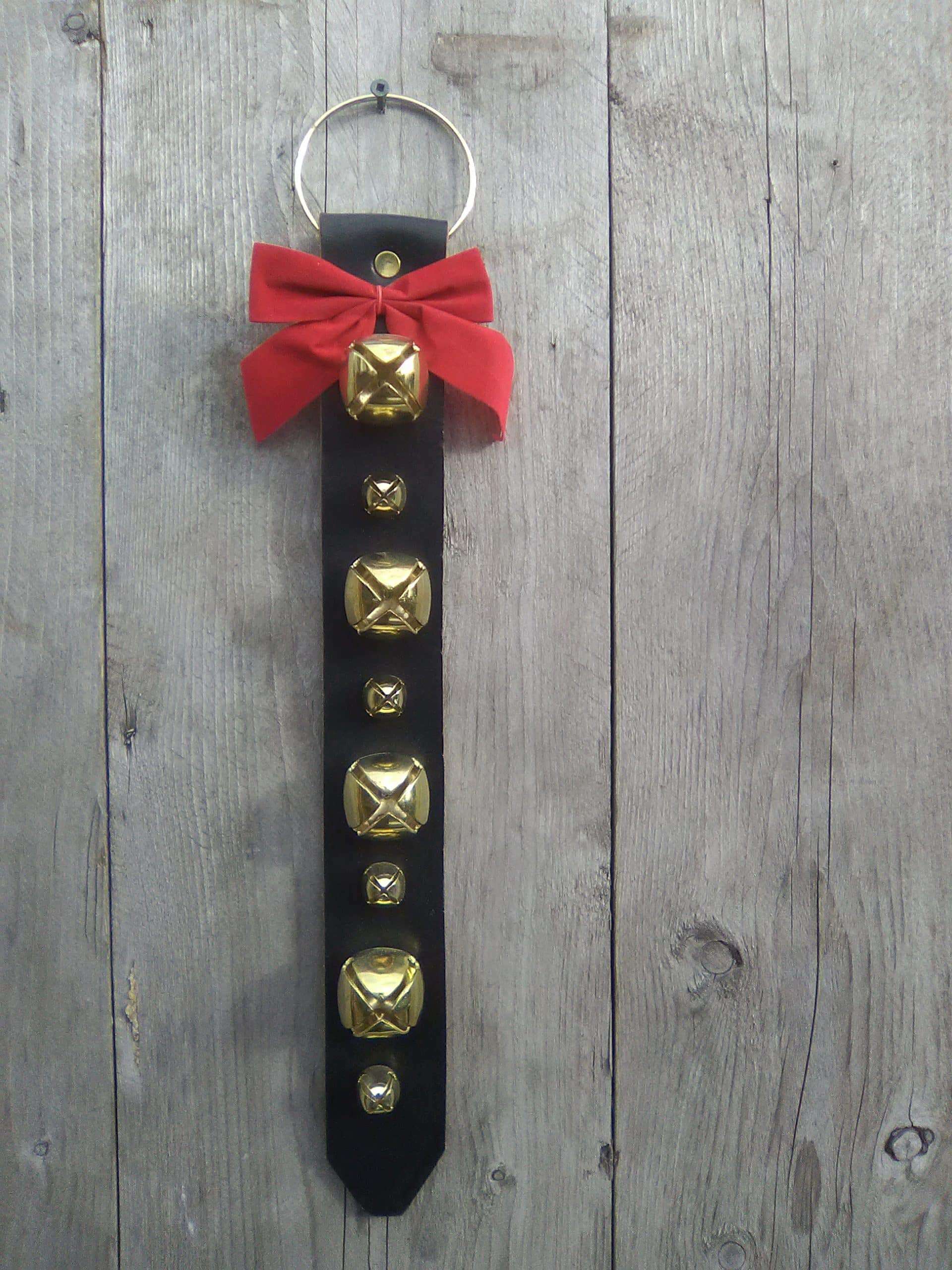 This door hanger is not only decorative but can help serve a purpose. You can hang it on a residential internal or external door, a commercial entrance, for instance. The bells ring when in motion. The thick black harness leather is stitched and lined with garment leather. The brass plated bells and ring are riveted onto the leather. Attached is also a red bow. Made in Kirkfield, Ont. Door hanger with 8 brass plated bells