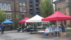 Four tents set up outside st anne's church with a small group of socially distanced famers market shoppers and workers