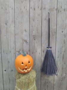 Black broom on stump next to carved jack o'lantern. Background is a wood wall